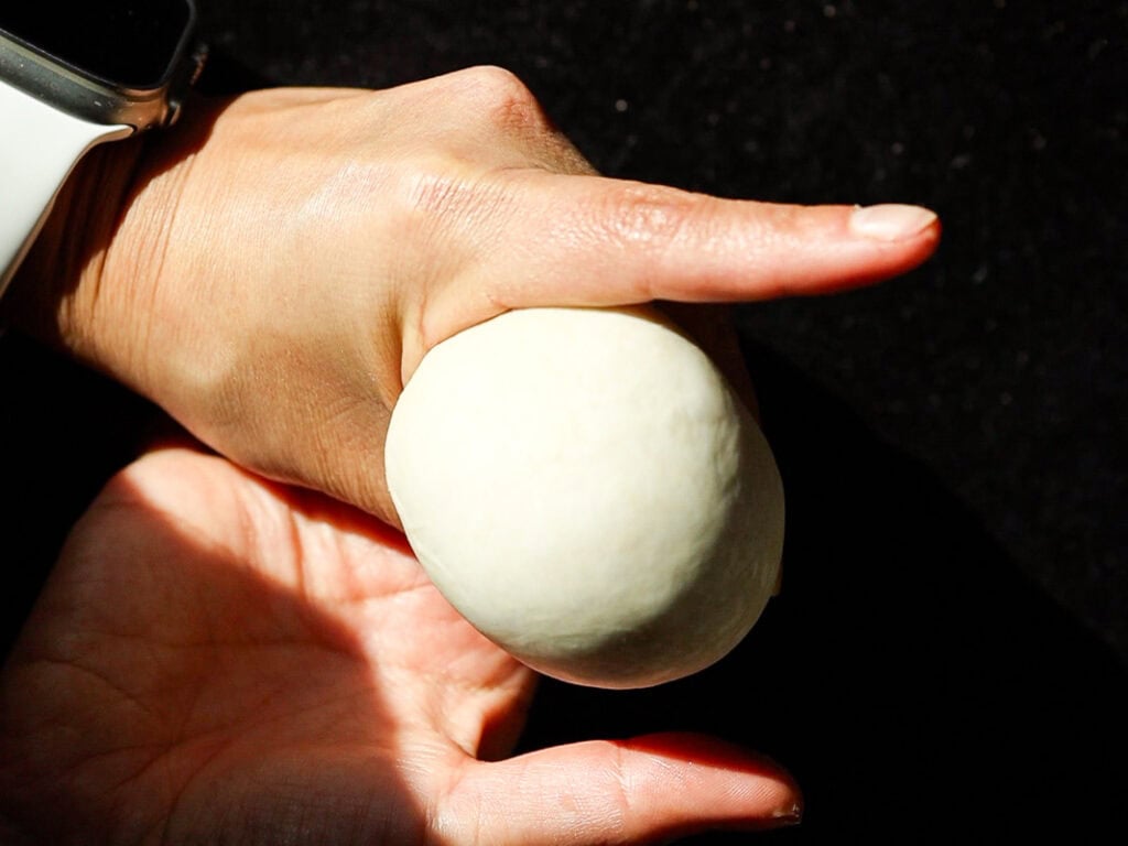 A person wearing a white smartwatch molds a ball of dough in their hands against a dark background.